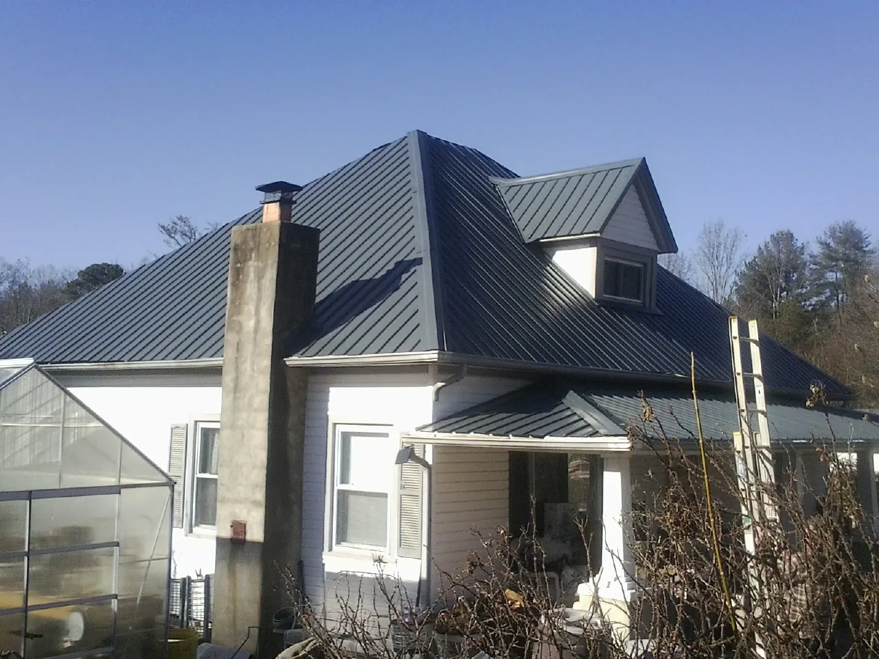 Dark blue standing seam metal roof on a white farmhouse with dormer — Slate & Tile Roof Repair by Roofing Brothers in East Nassau