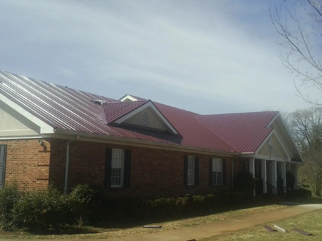 Red metal roof with gabled entries on a long brick building, from a Hail Damage Roof Repair job in East Nassau