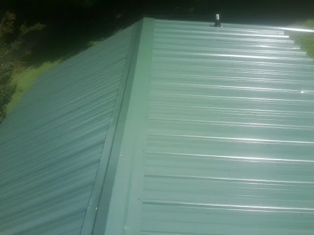 New green metal panels meeting at the ridge of a roof — Flat Roof Repair work by our crew in East Nassau