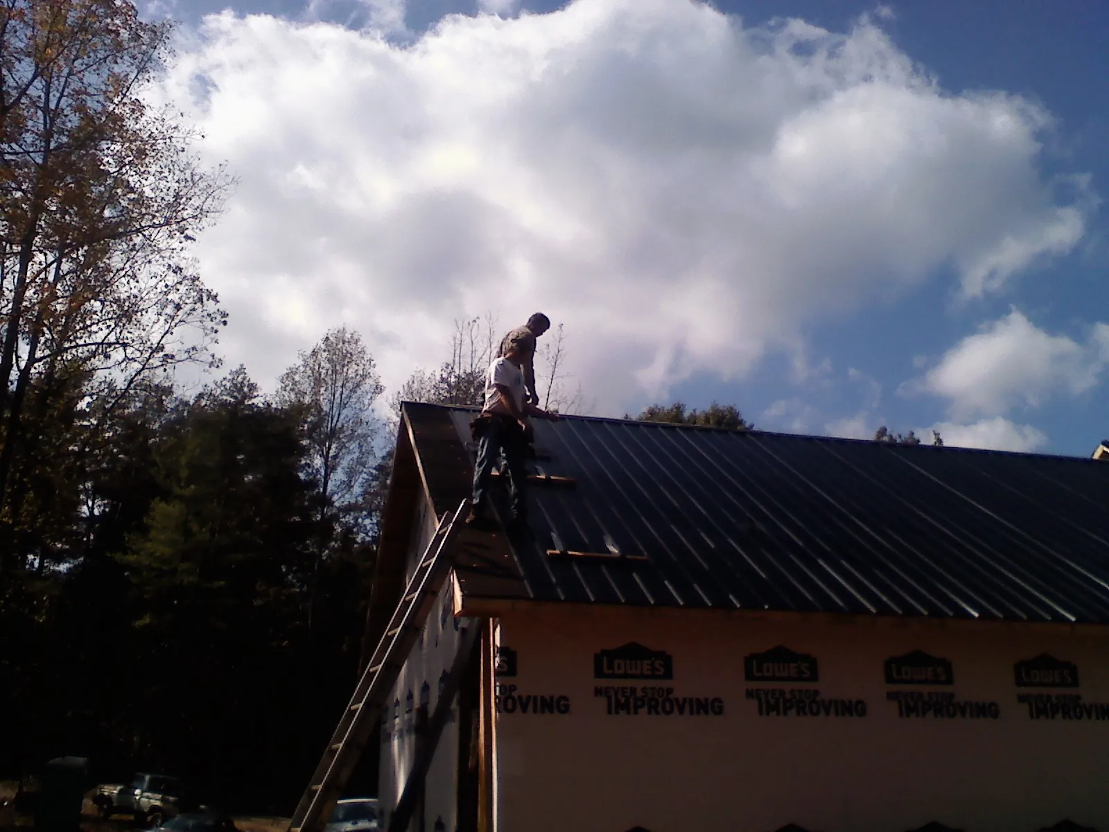 Roofer fastening dark metal panels high against a cloudy sky, from a Roof Inspection job in East Nassau
