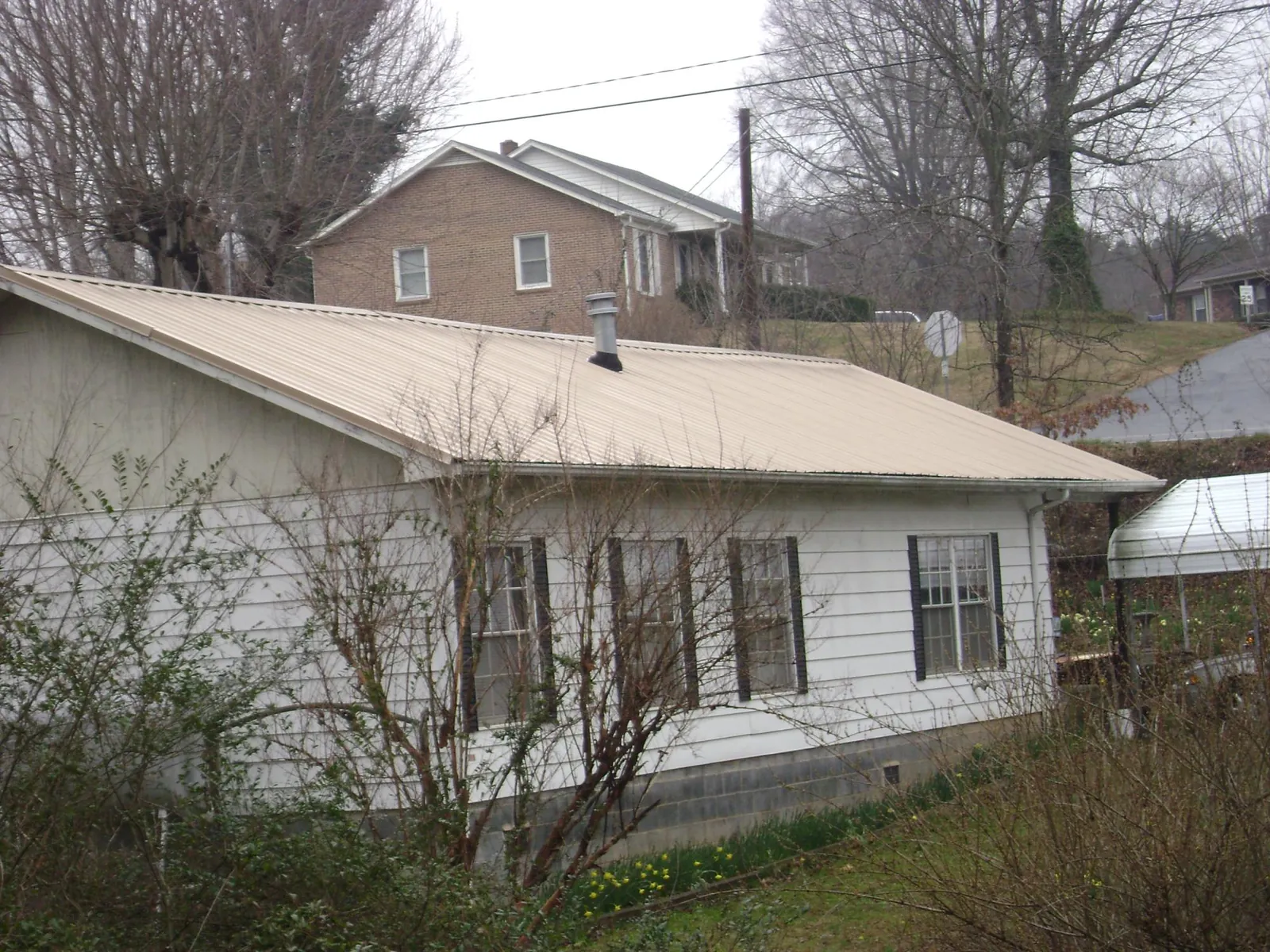 Tan metal roof on a white sided house set into a hillside — Commercial Roofing by Roofing Brothers in East Nassau